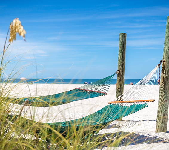 a relaxing scene of two hammocks strung between wooden posts on a sunny, white sand beach. 